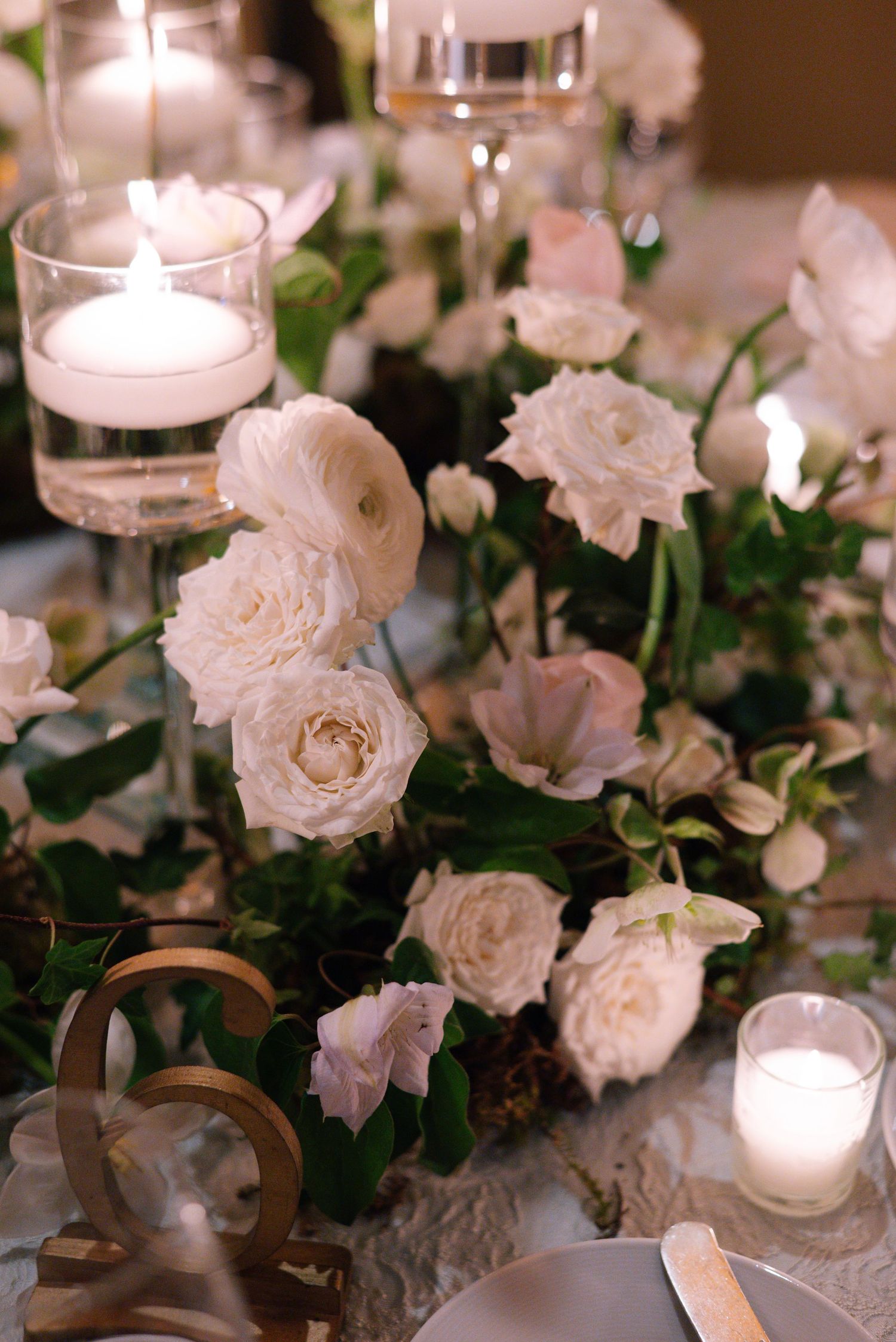 Elegant table setting with white roses and floating candles in glass votives on a textured tablecloth.
