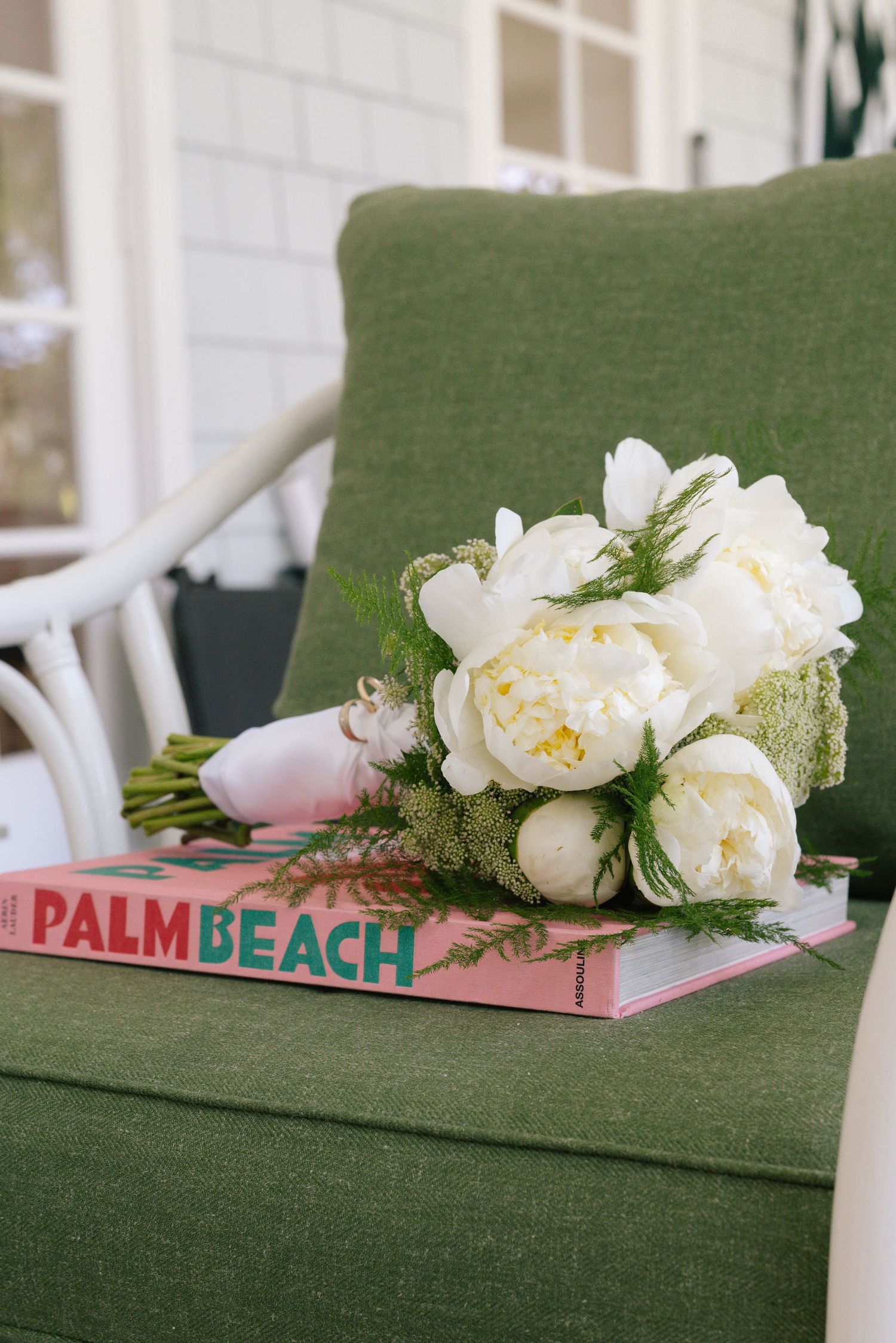 White peonies and Palm Beach coffee table book displayed on green upholstered furniture.