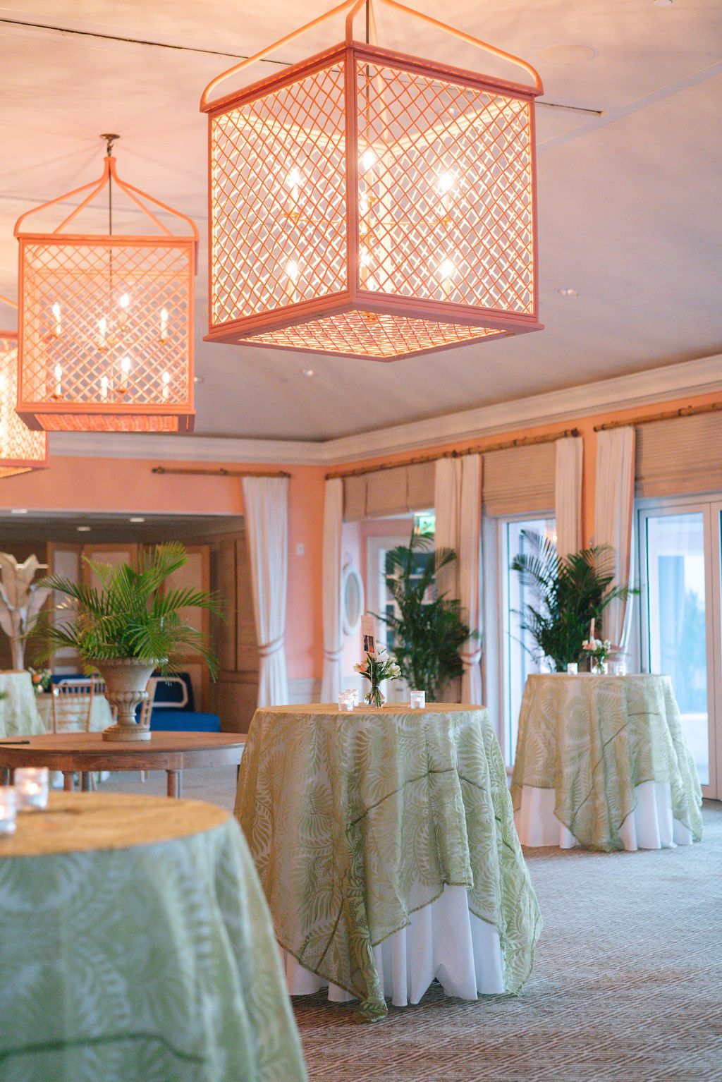 Elegant event space with coral-colored geometric pendant lights and sage green tablecloths.