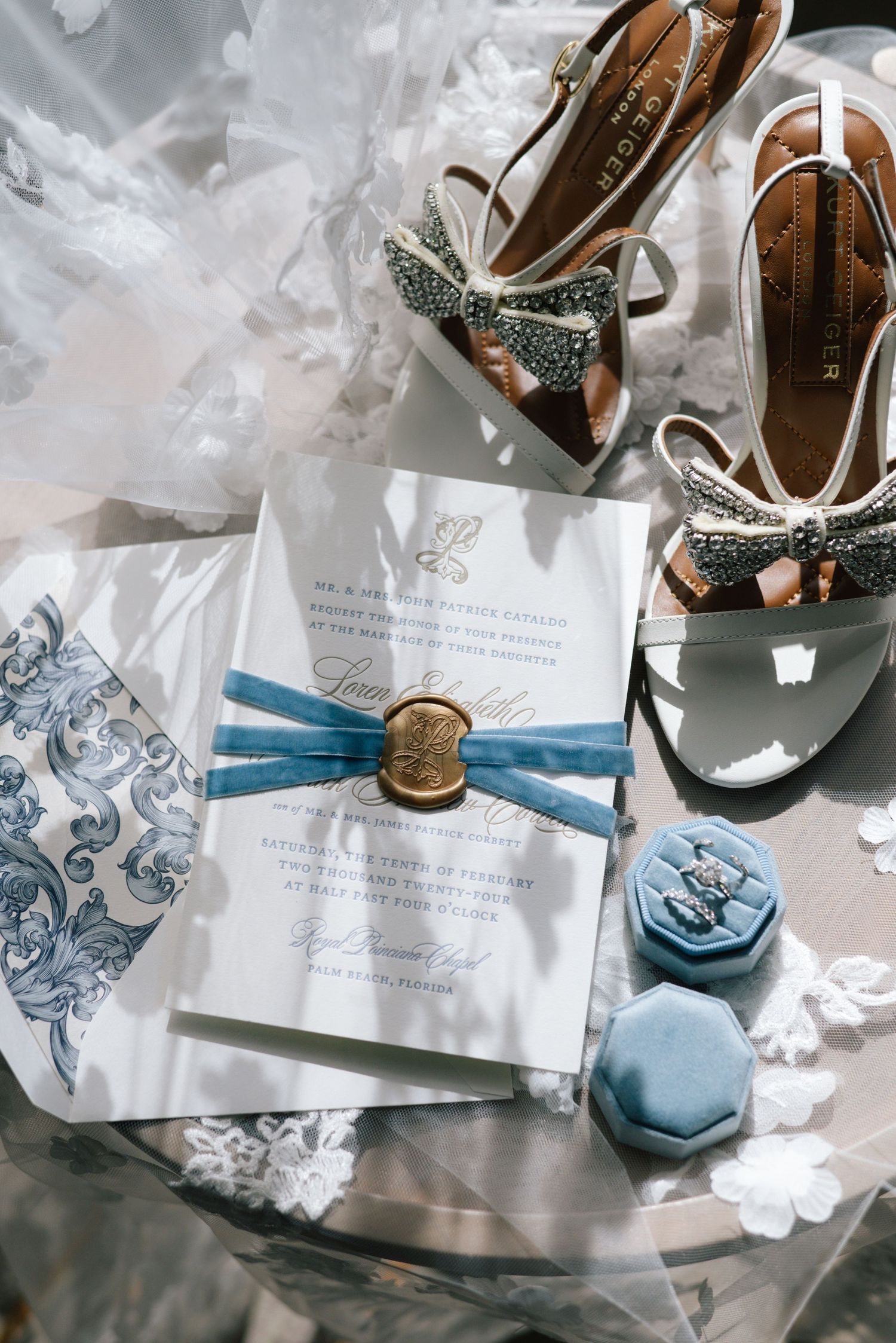 Elegant wedding invitation with blue ribbon and wax seal alongside sparkly bridal shoes and blue macarons.