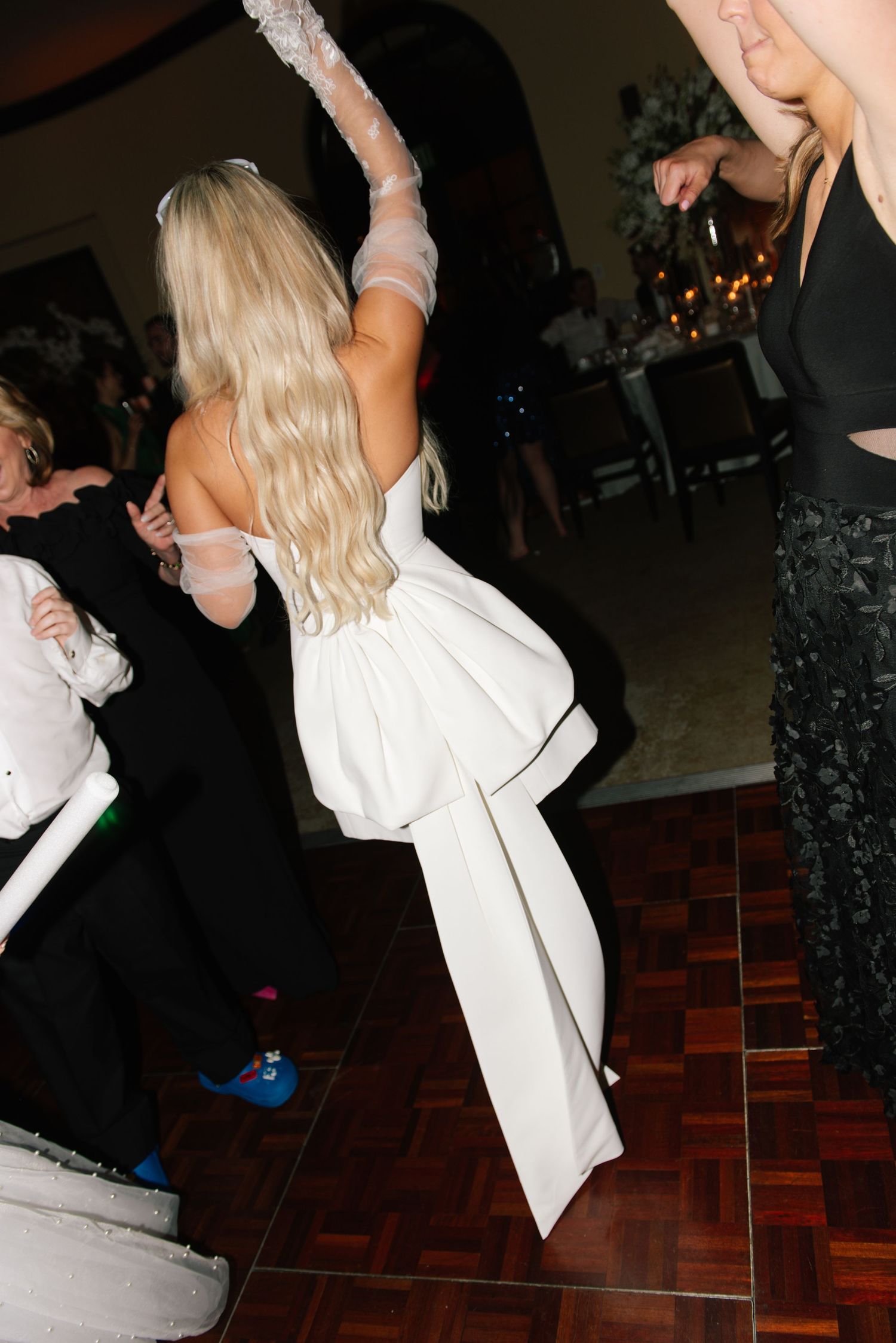 Bride in white dress dancing energetically on wooden dance floor at wedding reception.