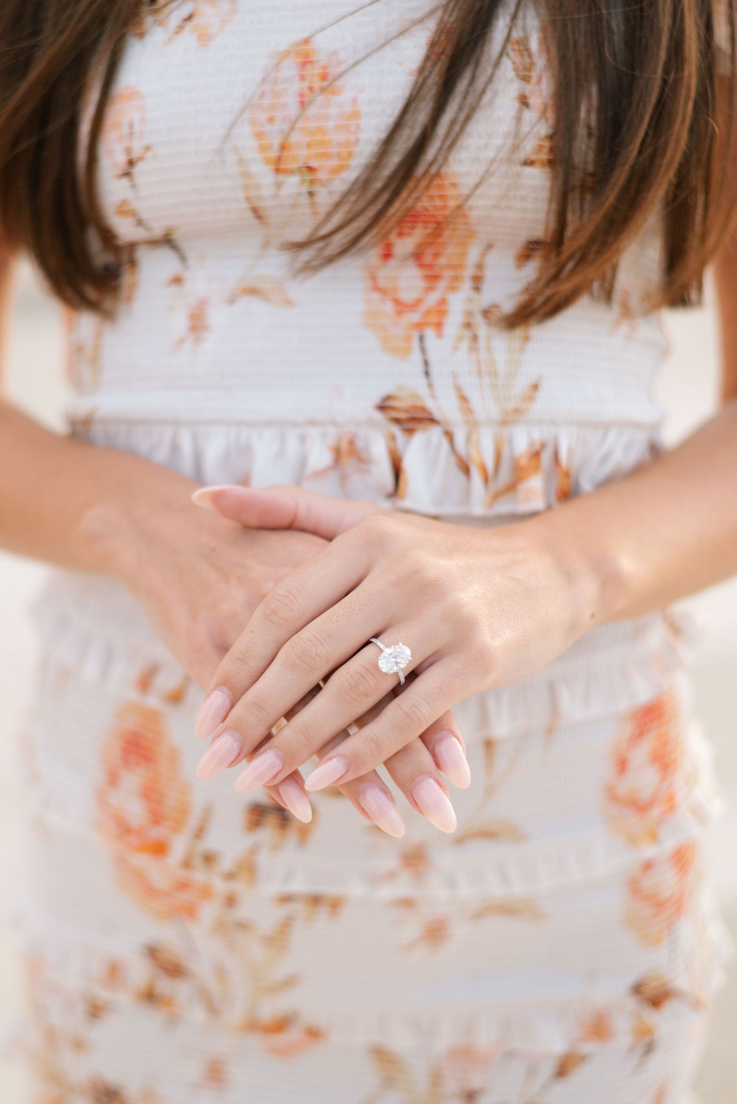 Close-up view of an engagement ring on a woman's hand wearing a white and peach floral patterned dress.