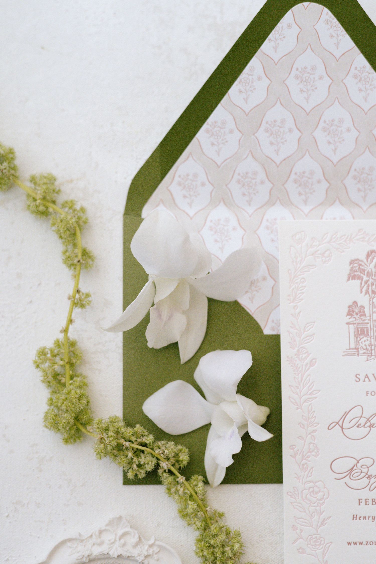 Elegant wedding invitation with green envelope, white floral pattern lining, and delicate white orchids.