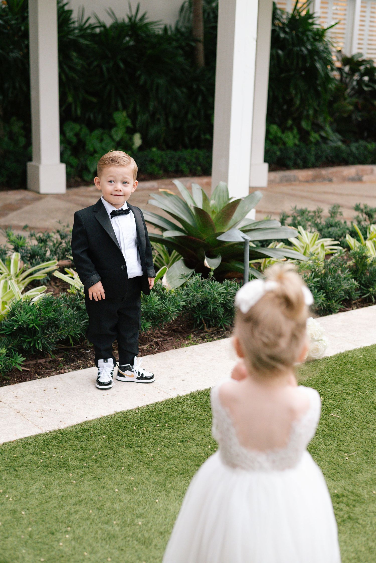 Wedding party lined up outdoors for formal photos with palm trees and white building in background.