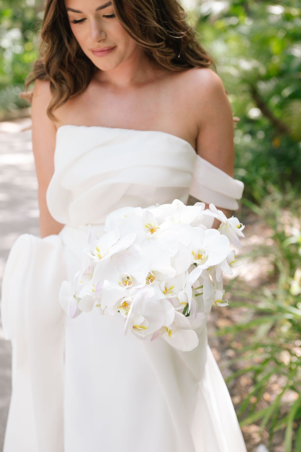 Off-shoulder white wedding dress adorned with delicate white orchids.