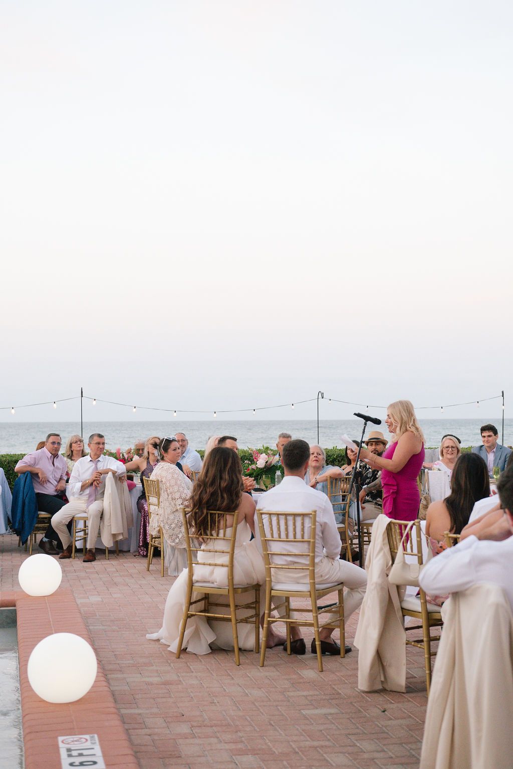 Wedding reception seating arrangement with white chairs and string lights at a waterfront venue.