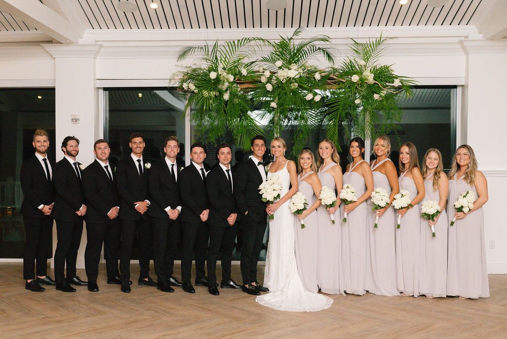 Wedding party members in black and white attire pose formally inside elegant venue.