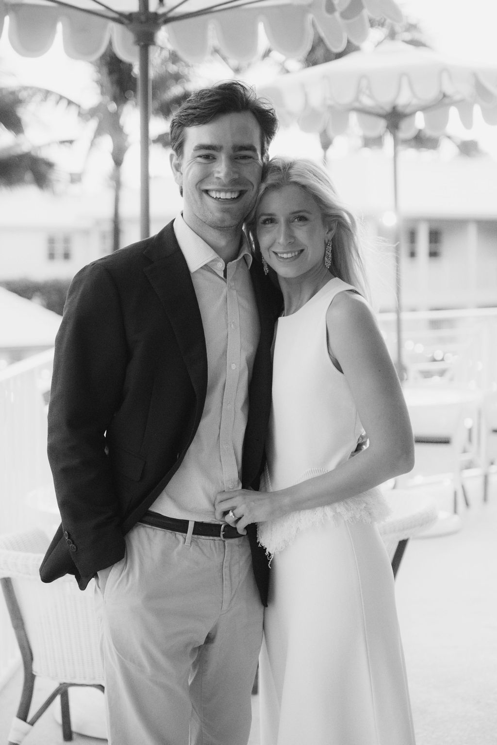 Black and white portrait of a couple under decorative umbrellas on a seaside terrace.