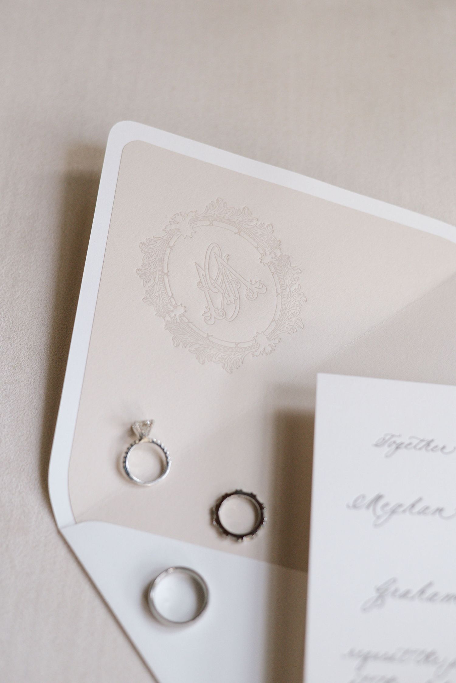 Wedding rings and monogrammed stationery displayed on cream-colored envelope.