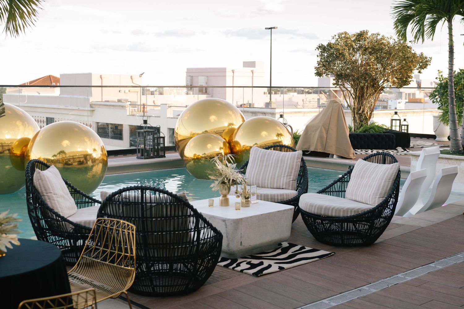Modern outdoor lounge area with black wicker chairs and large golden spherical decorations by the pool.