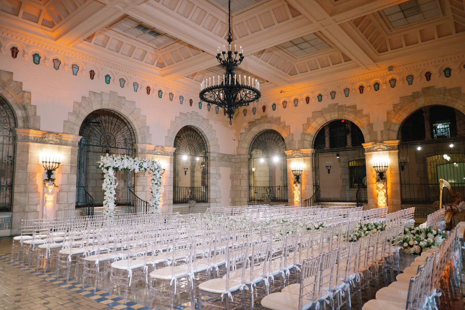 Grand wedding ceremony hall with ornate arches, crystal chandelier, and white floral altar.