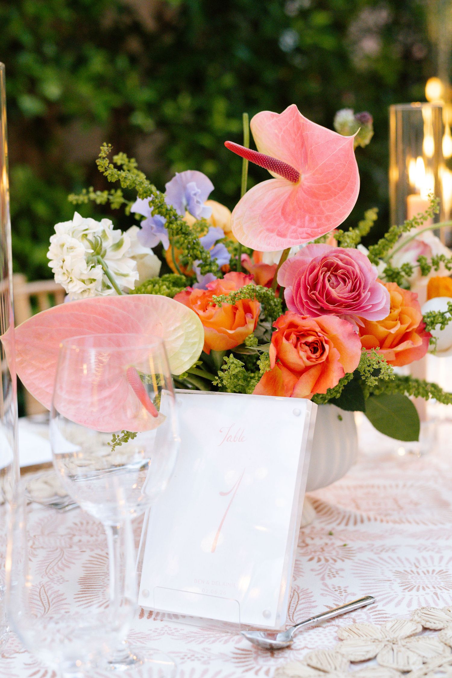 Coral and pink floral centerpieces with roses and anthurium on white tablecloth.