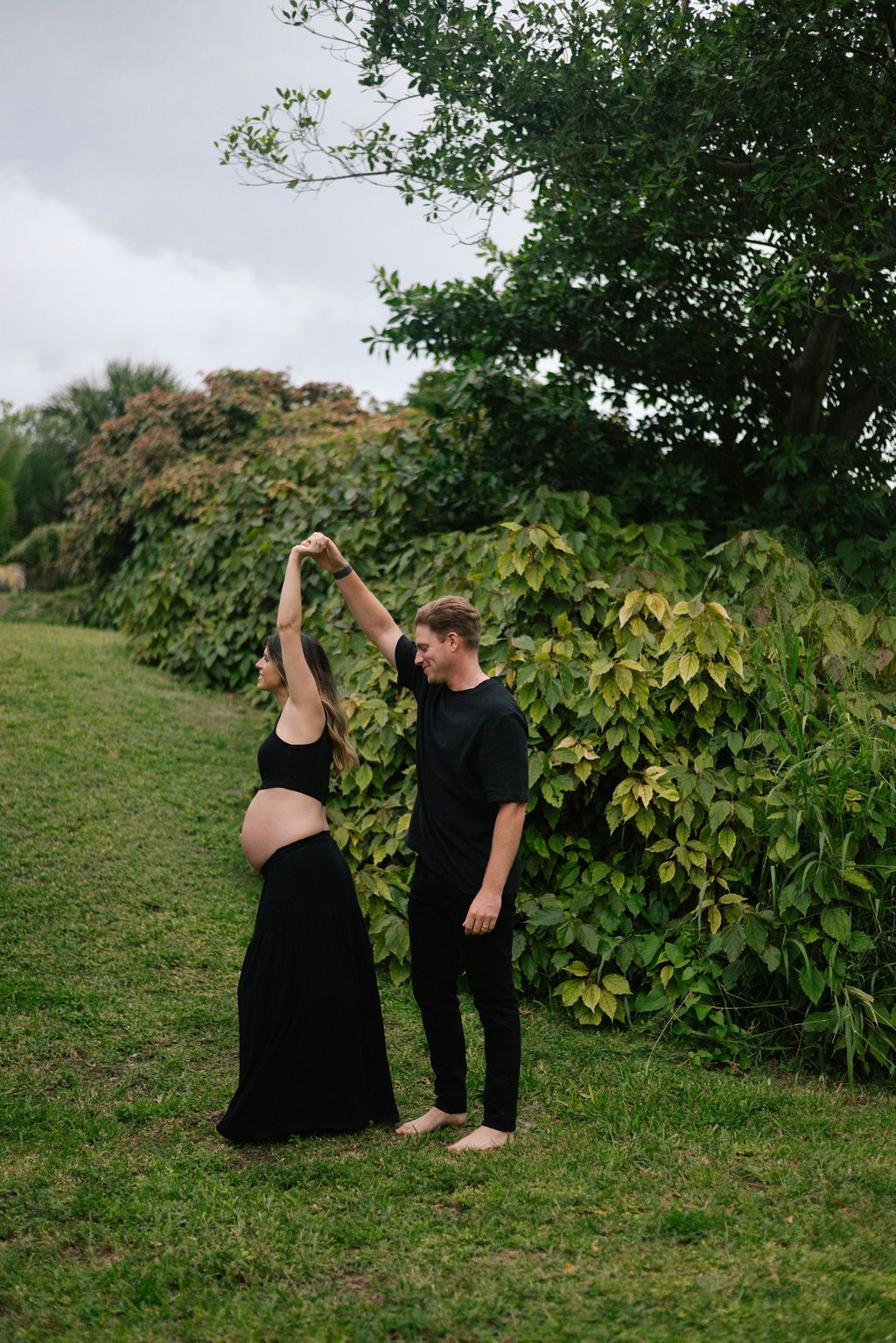 Couple in black clothing dances together on a green hillside surrounded by trees.