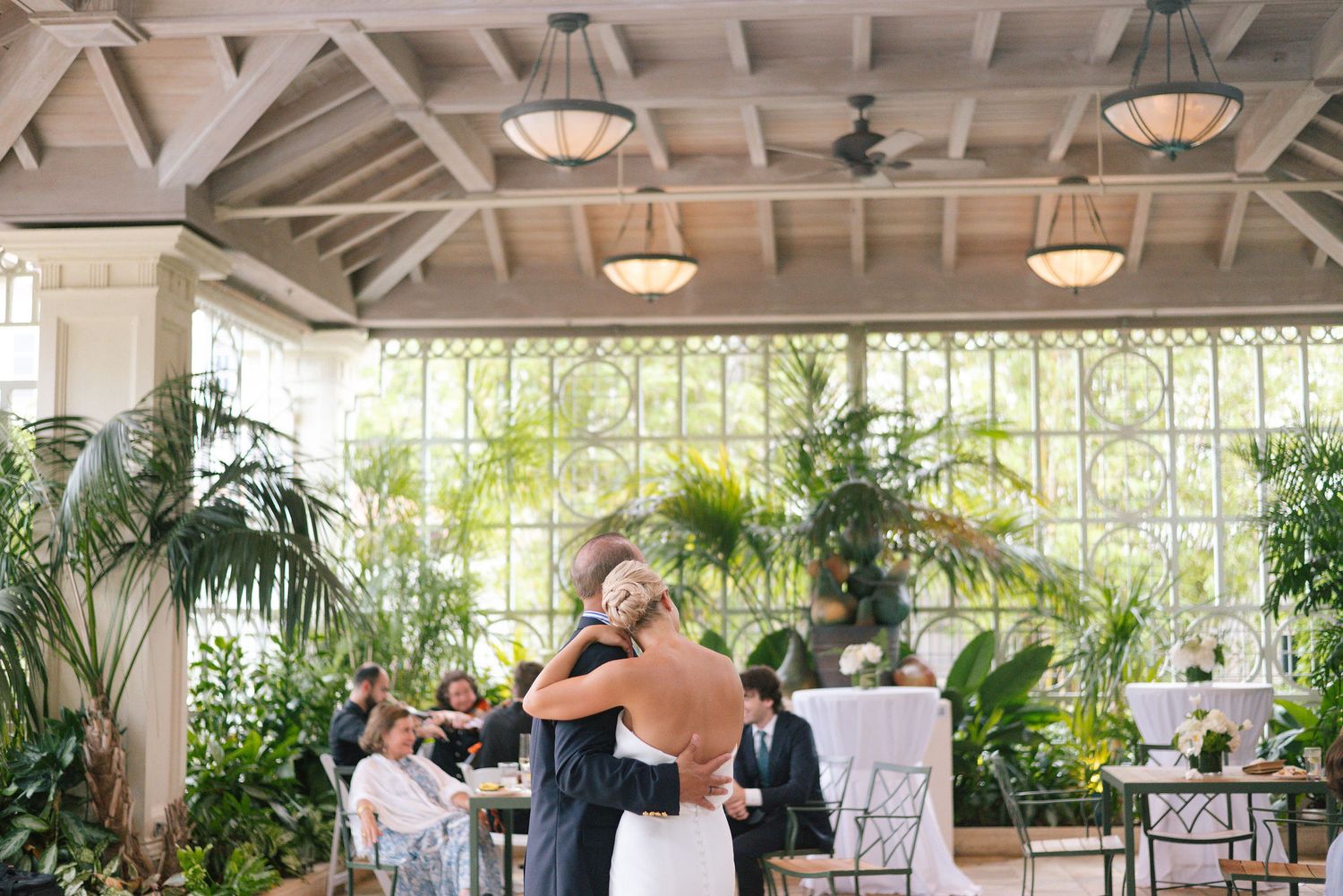 Wedding dance in a bright conservatory with vaulted ceilings and tropical plants.