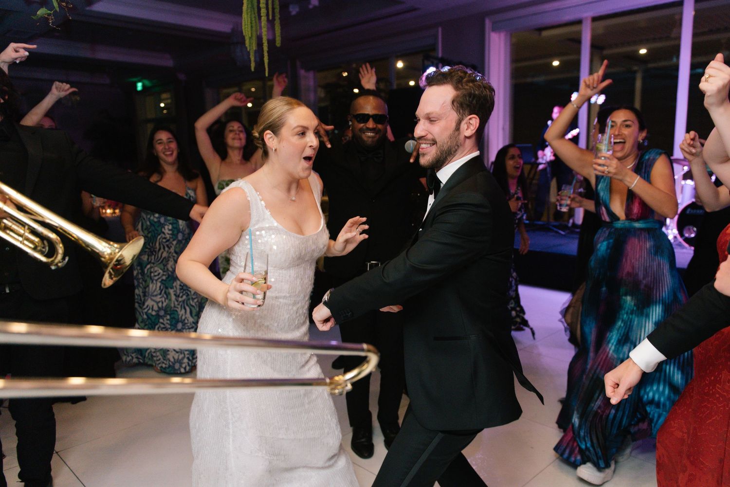 Newlyweds dance energetically at their wedding reception surrounded by celebrating guests.