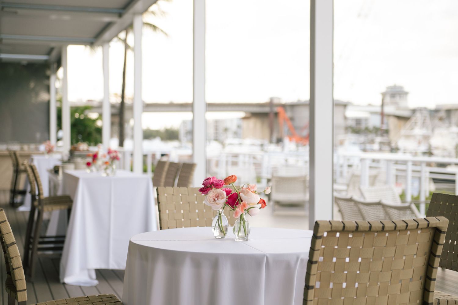 Coastal wedding reception venue with woven chairs and white tablecloths.