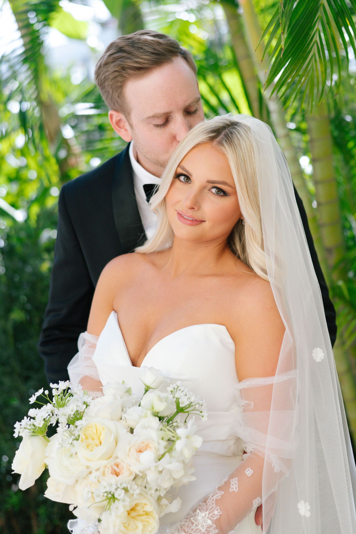 Elegant bride holds a lush white and cream bouquet surrounded by tropical palm trees.