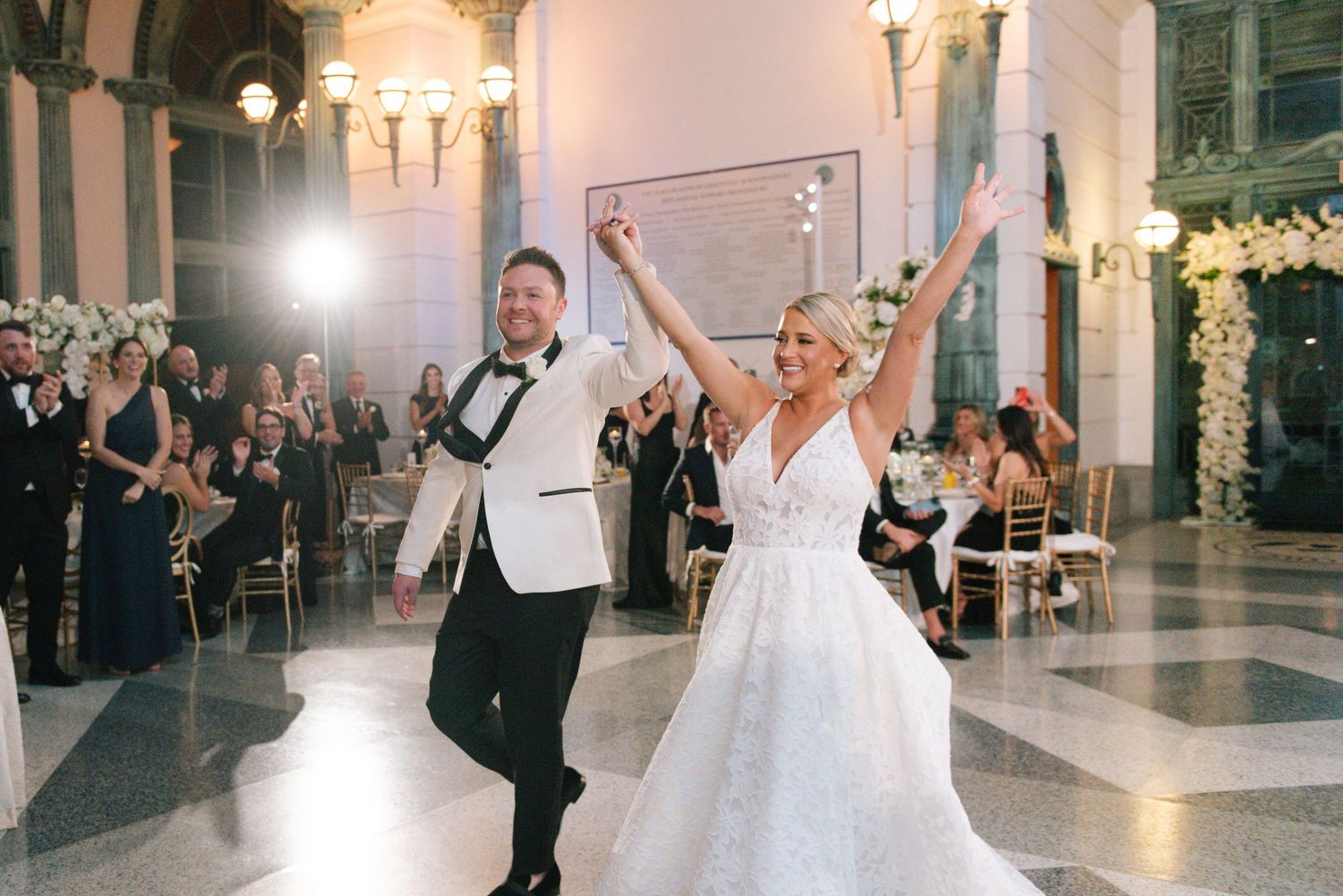 Joyful bride and groom make grand entrance into elegant ballroom wedding reception.