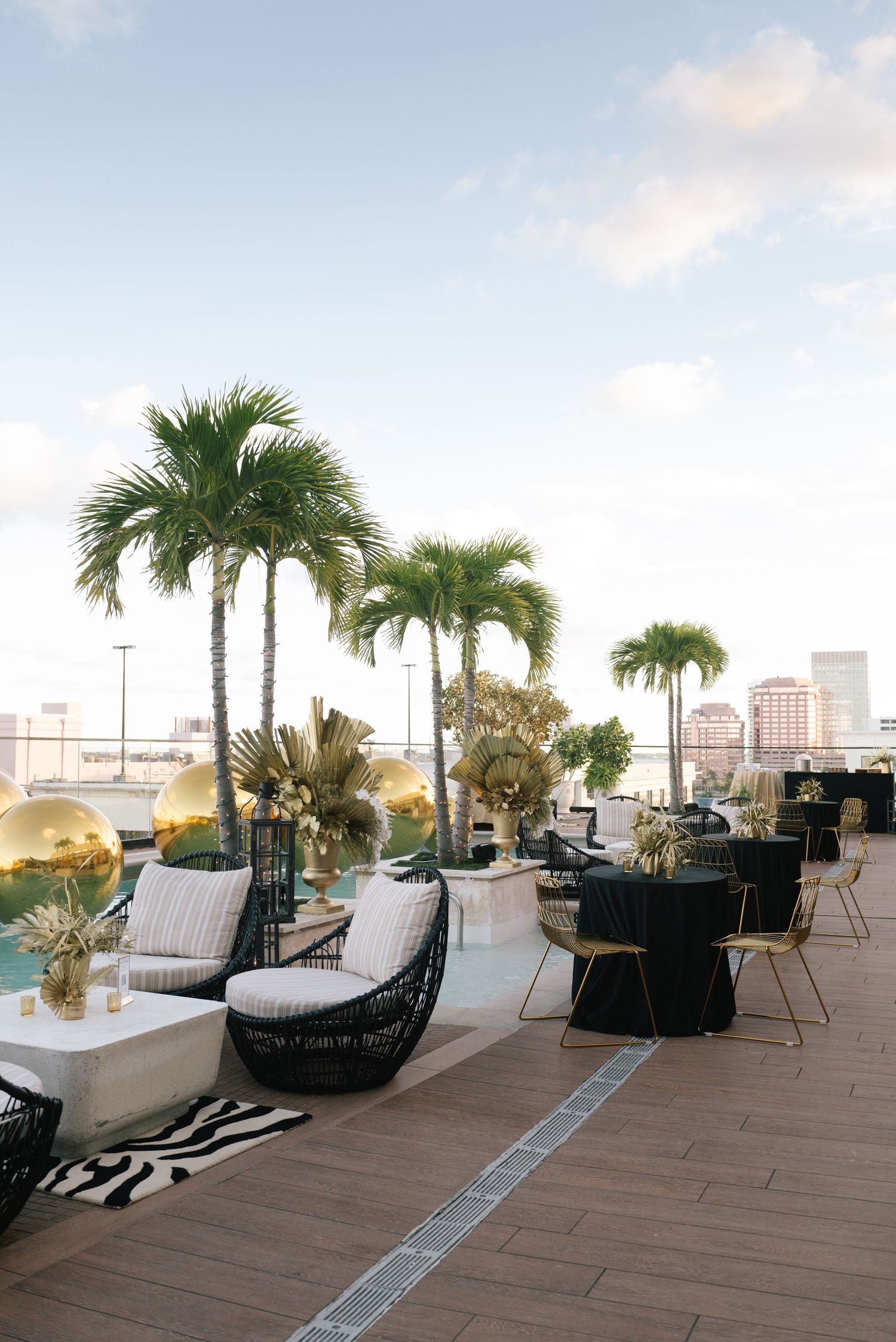 Luxurious rooftop venue with palm trees and modern lounge furniture overlooking a waterfront cityscape.