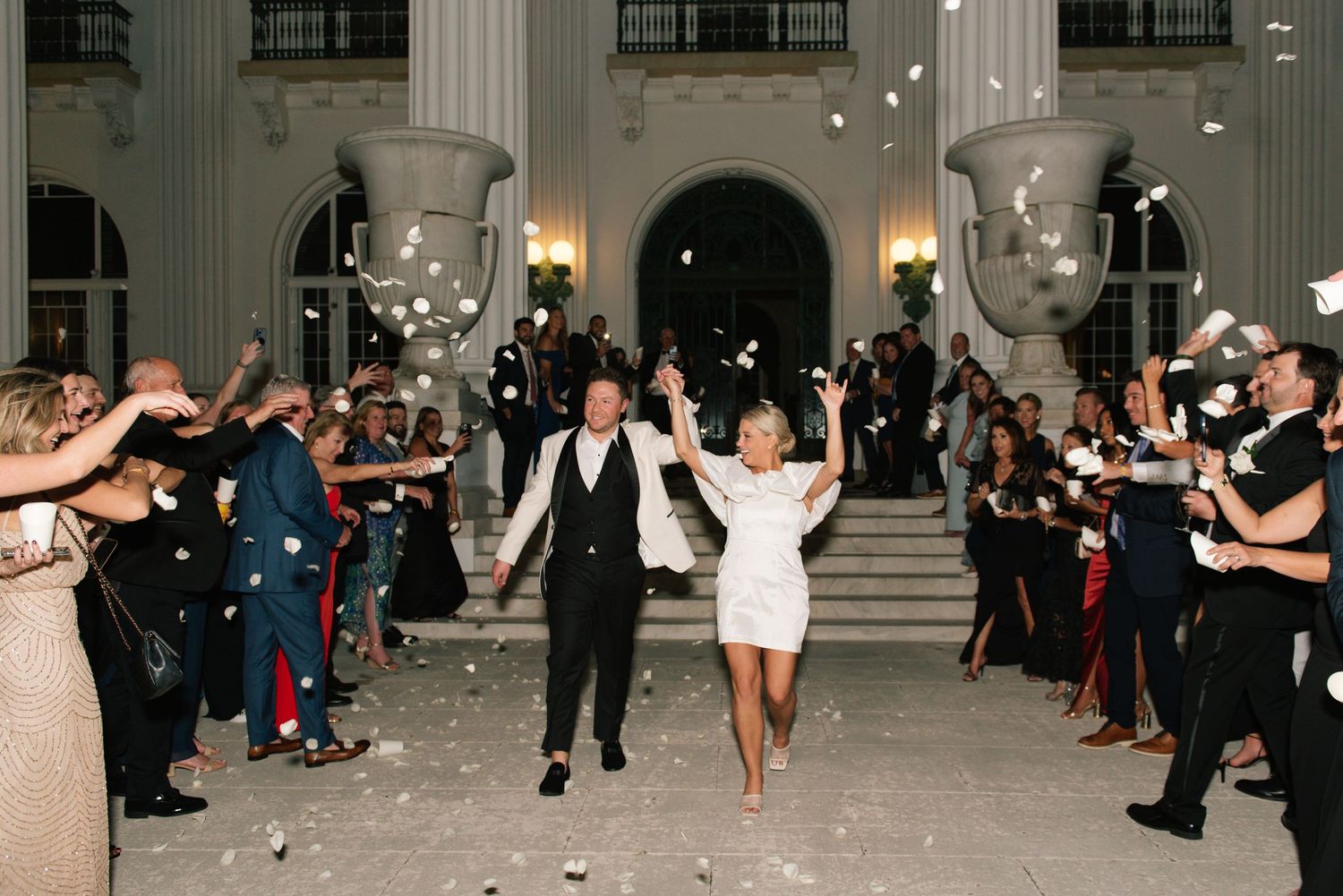 Bride and groom celebrating grand exit with confetti outside illuminated venue at night.
