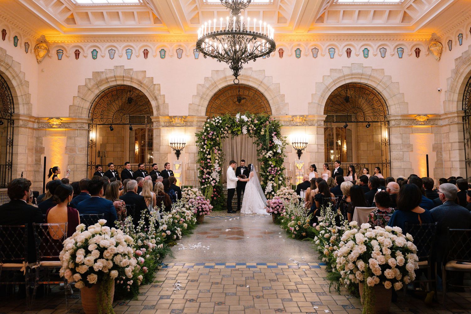 Luxurious indoor wedding ceremony space with white floral arrangements lining the aisle.