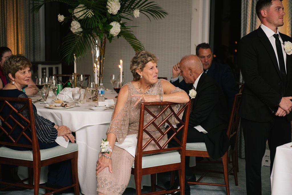 Guests enjoy conversation at an elegant wedding reception with white floral centerpieces and candlelight.