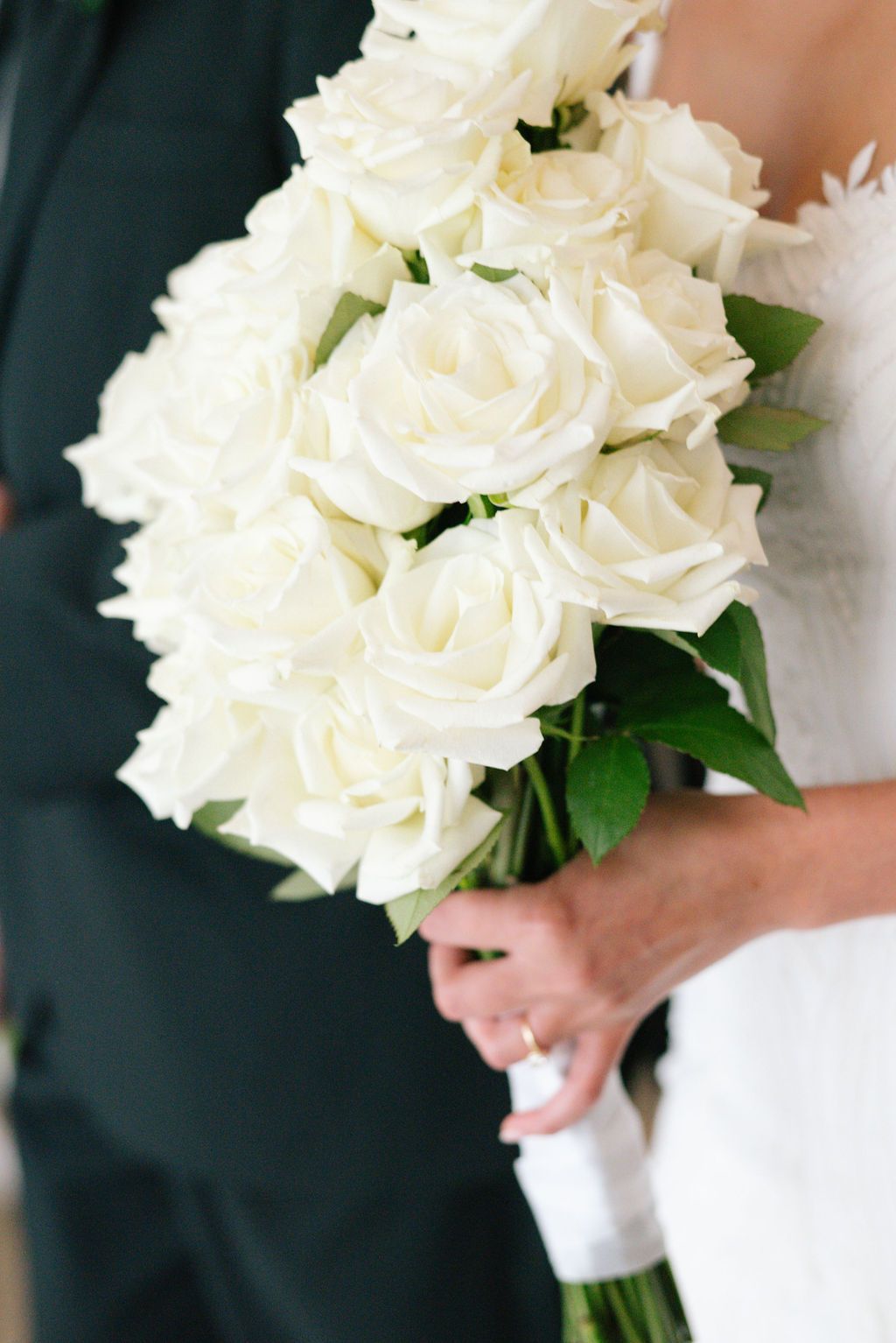 Close-up shots of elegant white rose wedding bouquets against black suits.