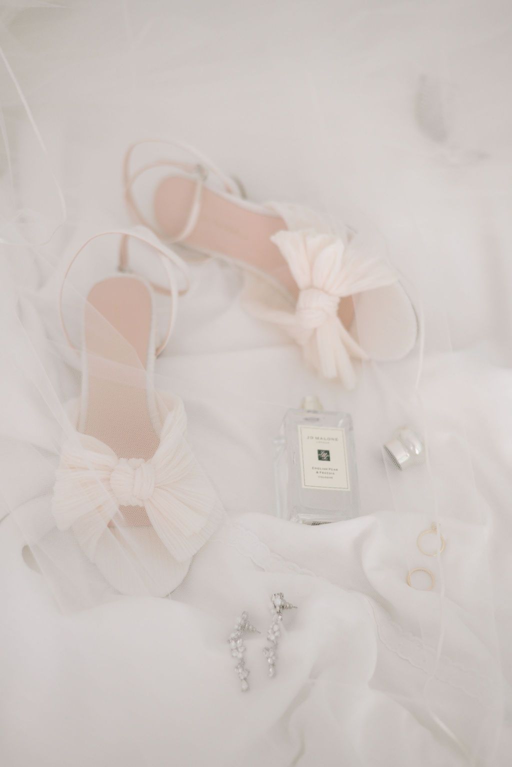 Ethereal arrangement of pink ribbons and perfume bottles on white tulle fabric.