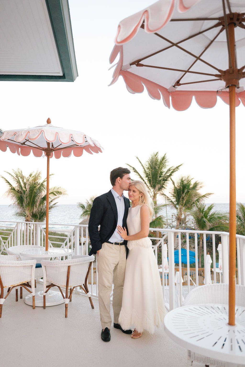 Romantic moment on an elegant balcony with decorative pink umbrellas and coastal scenery.