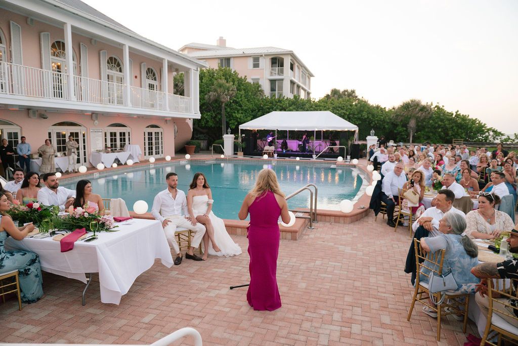 Wide shot of an outdoor wedding reception setup with tables and chairs near a swimming pool.