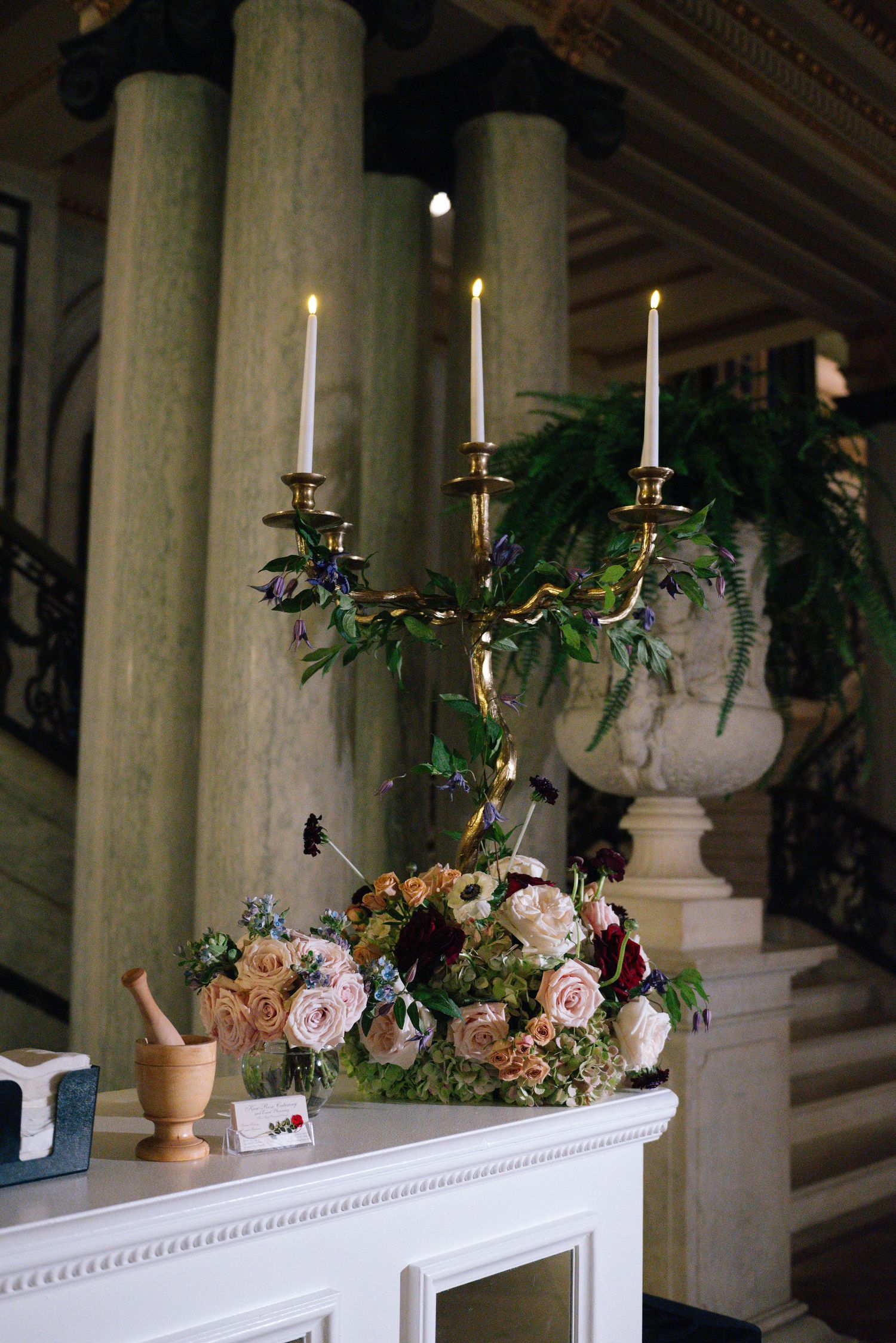 Ornate candelabra with floral arrangement featuring roses and greenery on white mantelpiece.