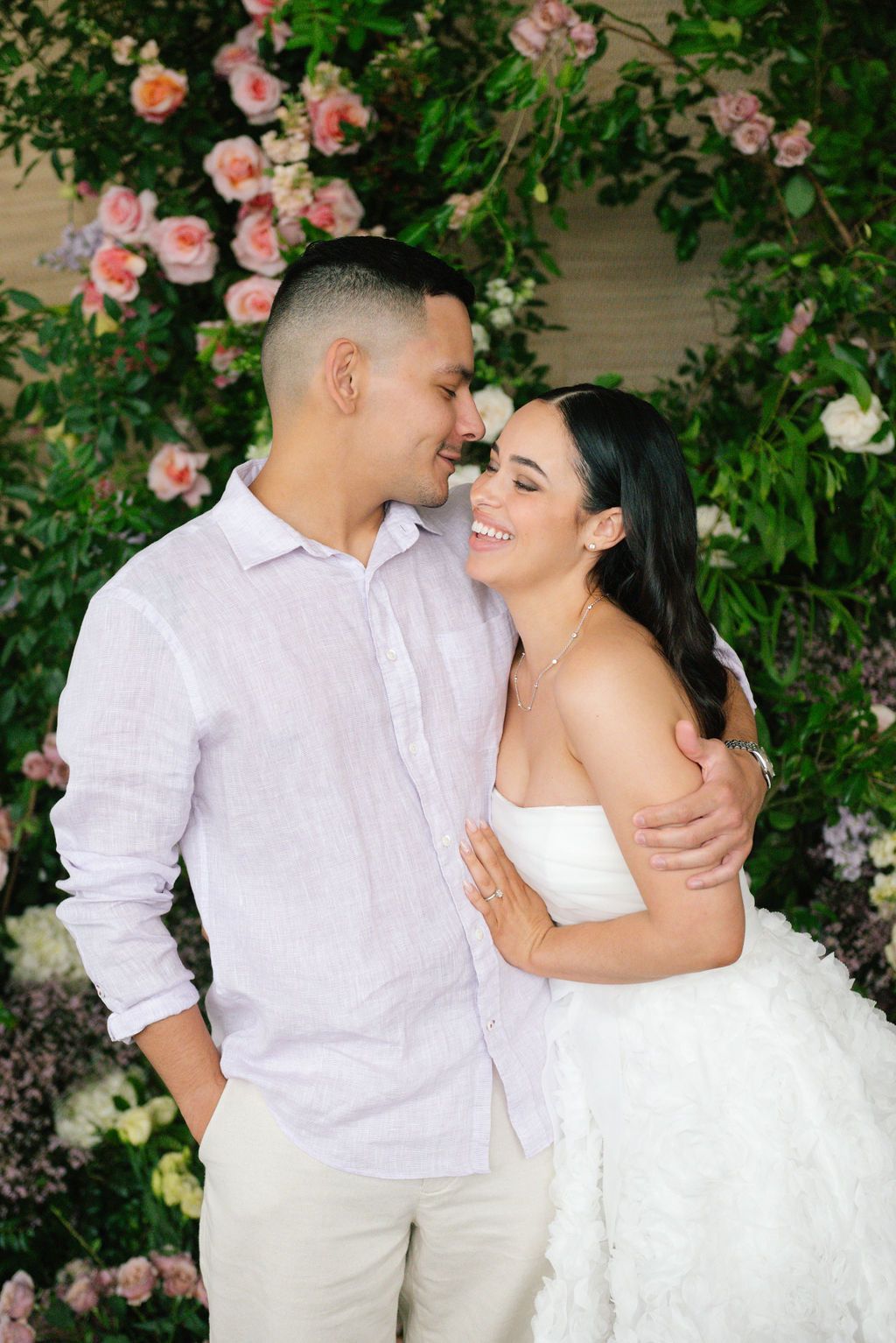 Romantic couple sharing intimate moment against backdrop of blooming pink roses.