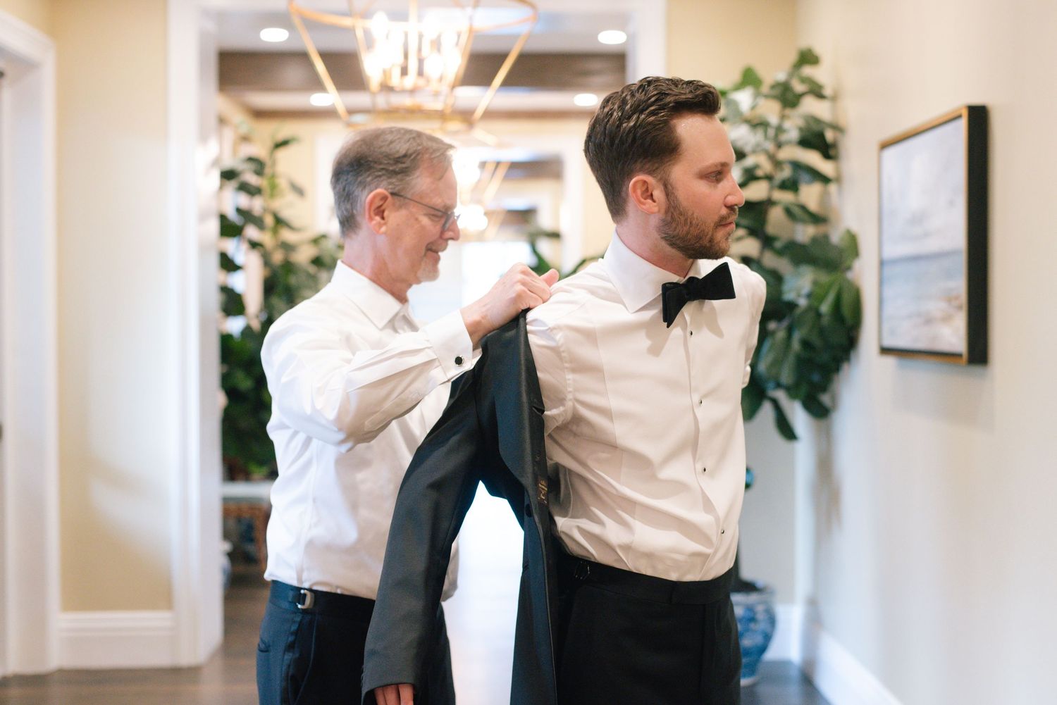 Guests in formal attire gather and mingle in an elegant indoor venue with white walls and decorative artwork.