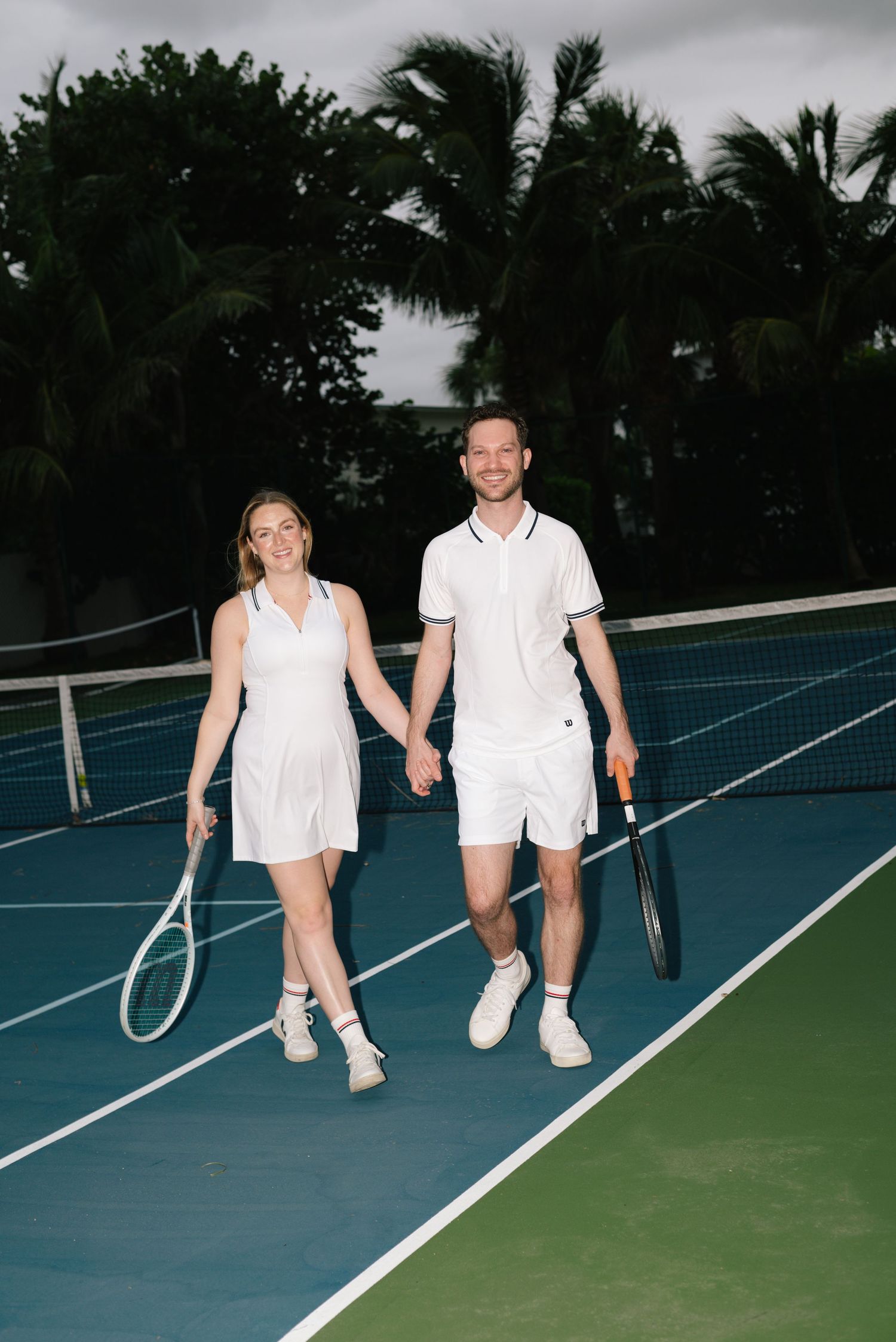 Athletic couple sitting together on blue tennis court with rackets.