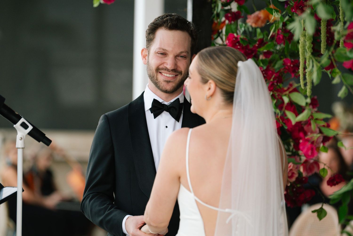 Couple exchanges vows under stunning red floral arch during ceremony.