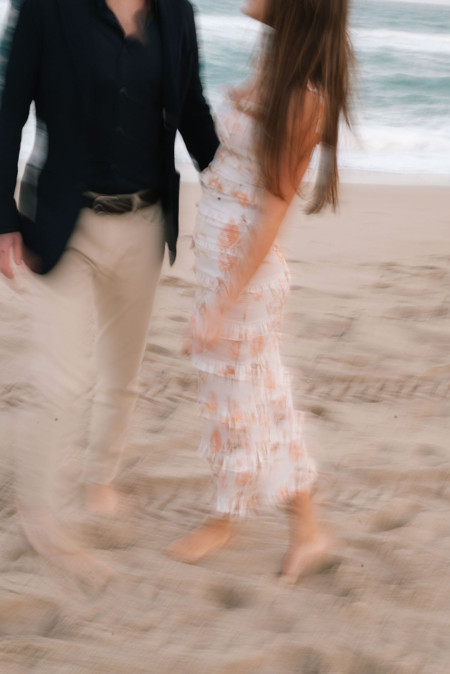 A couple walking together on a sandy beach with ocean waves in the background.