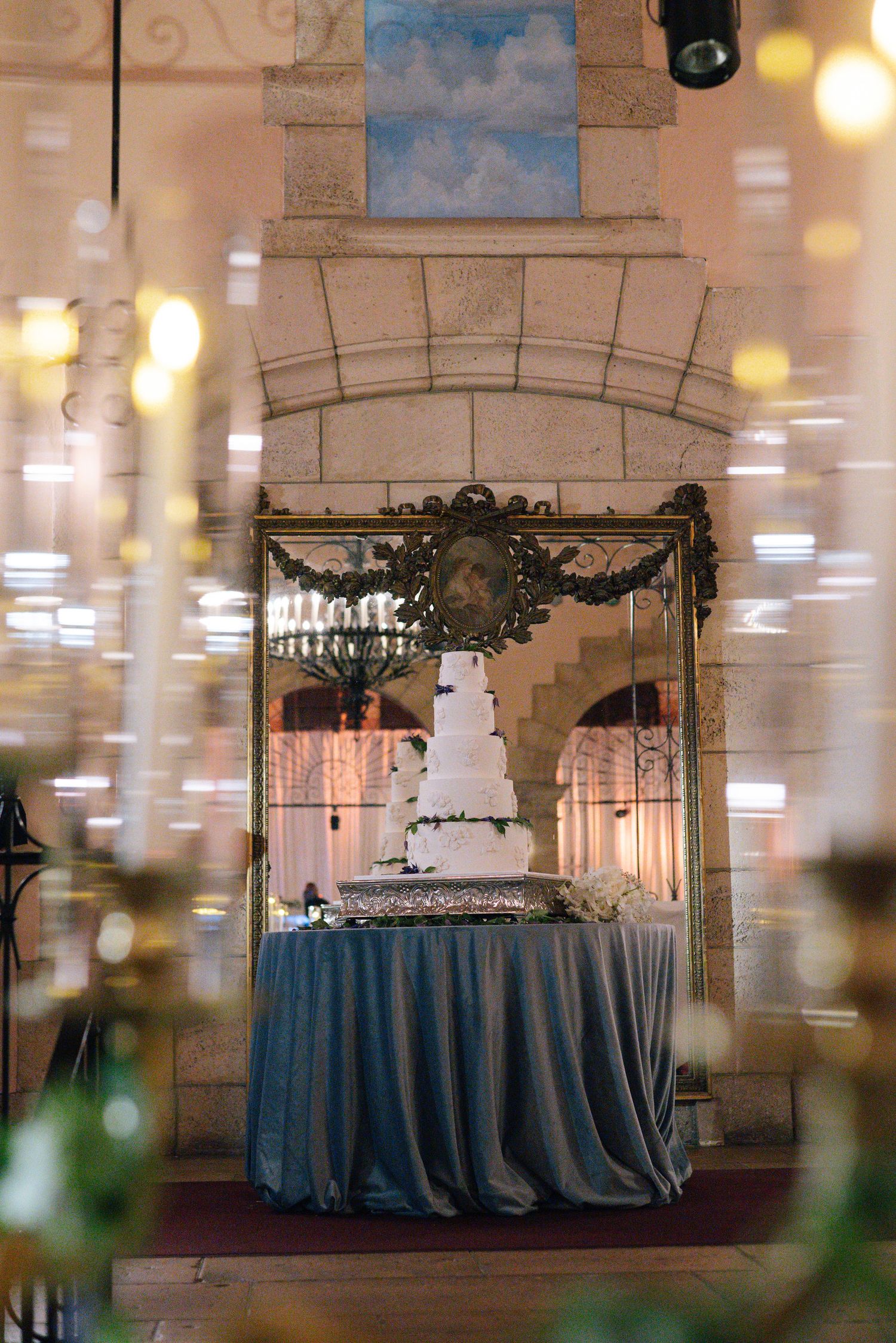 Wedding cake display on round table with blue tablecloth in an elegant stone archway setting.
