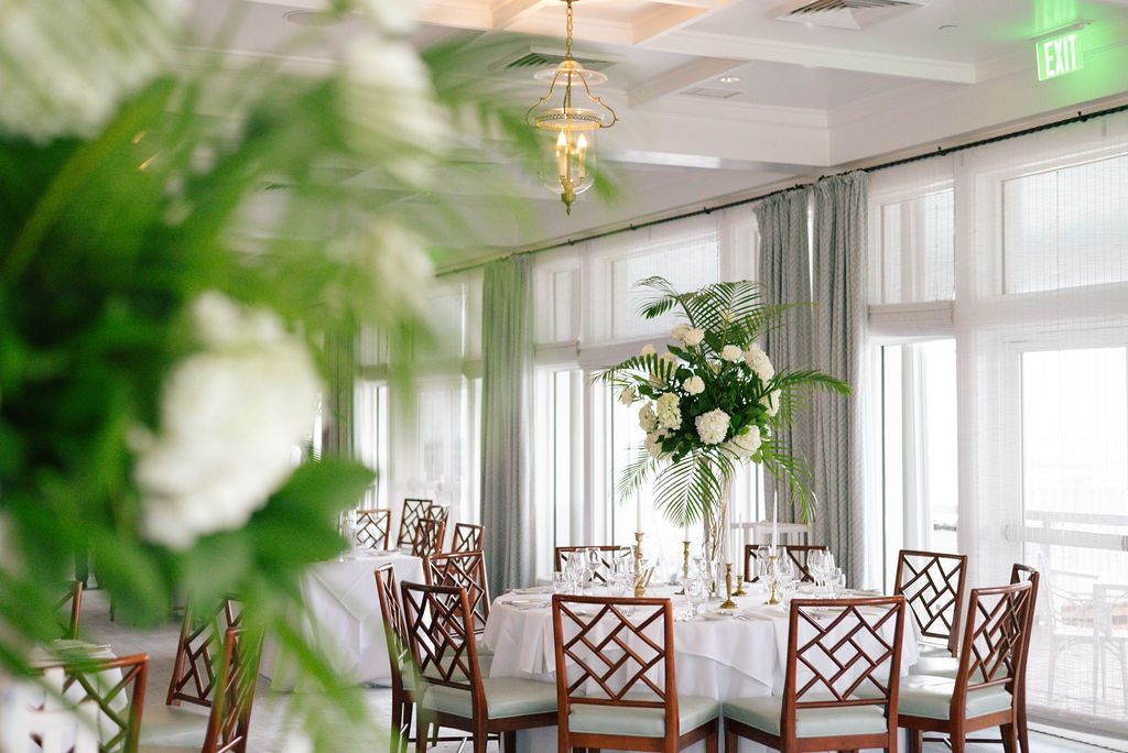 Reception venue with tropical greenery, white tablecloths and geometric wooden chairs.