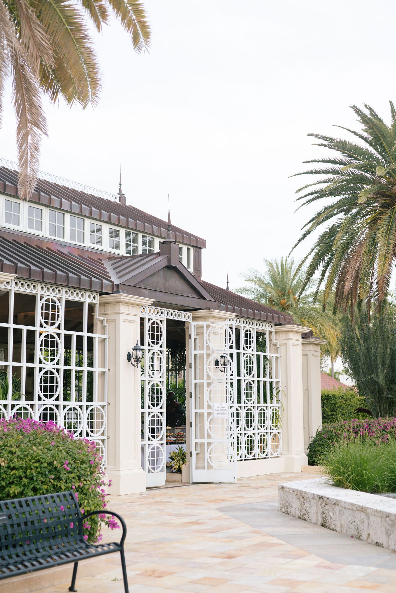 Elegant white colonial-style building exterior with ornate windows and palm trees framing the entrance.