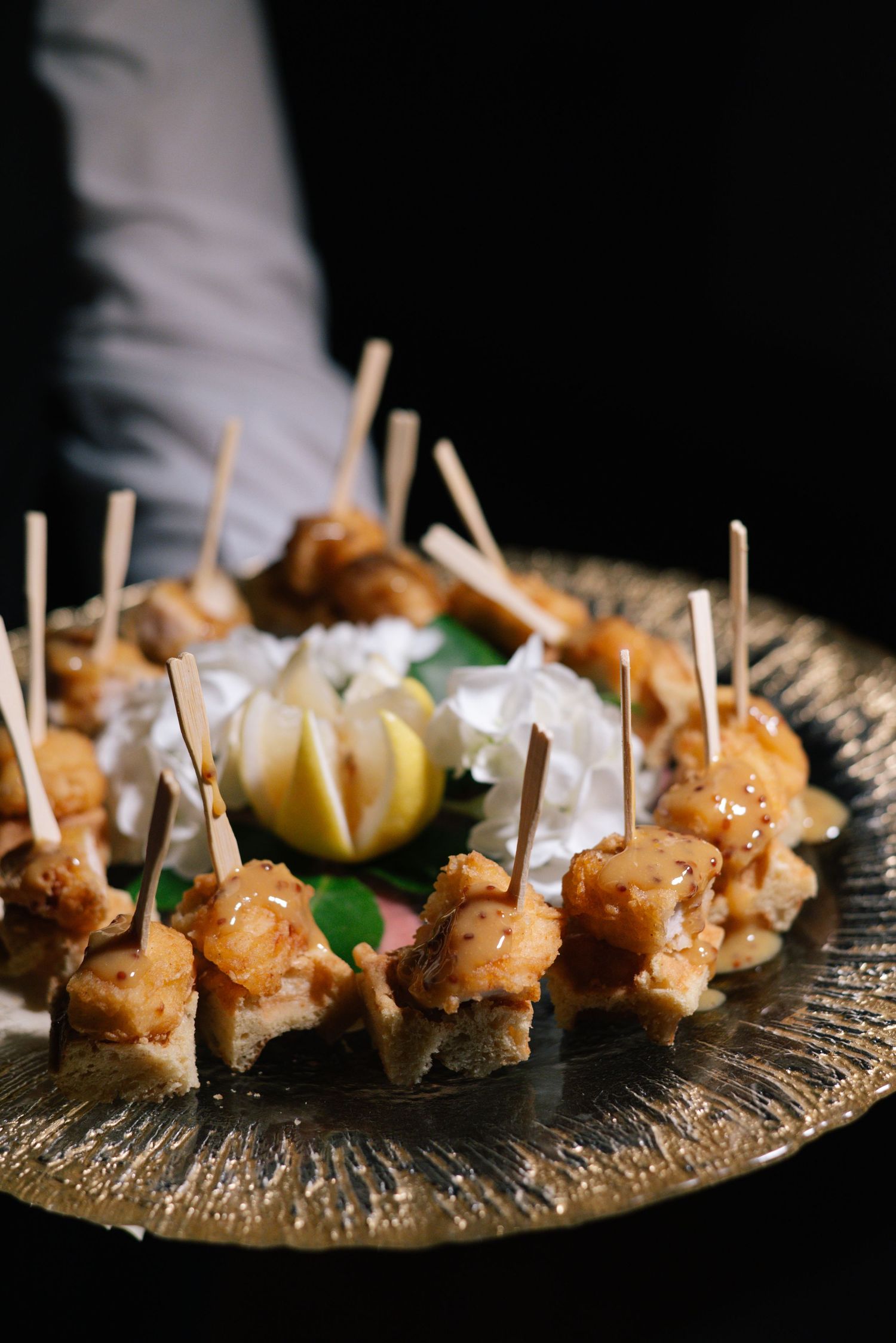 Golden platter of glazed chicken skewer appetizers served at elegant wedding reception.
