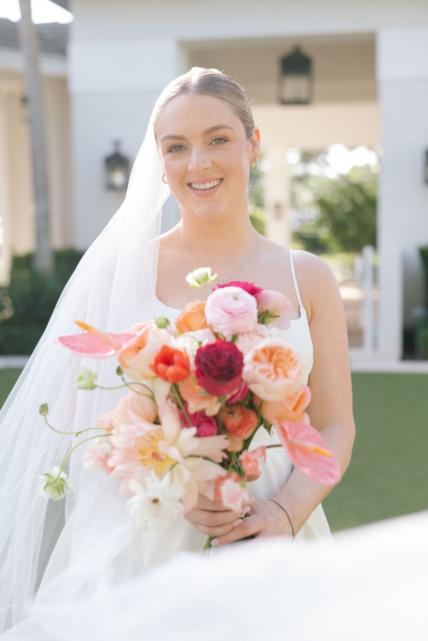 Beautiful bridal portraits showcasing vibrant coral and pink bouquets against a white wedding gown in natural light.