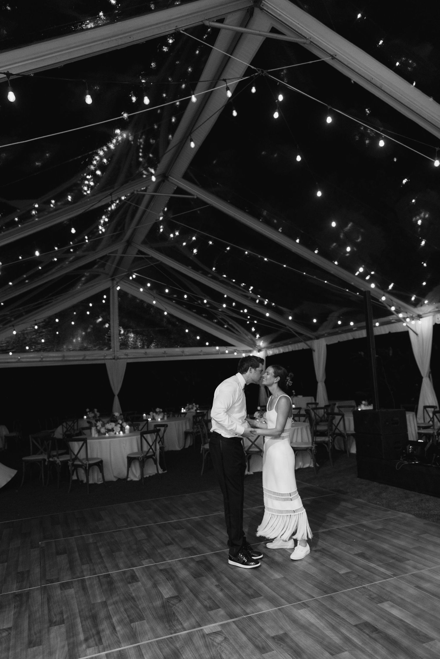 Couple sharing a romantic dance under twinkling lights in a clear-top tent at night.