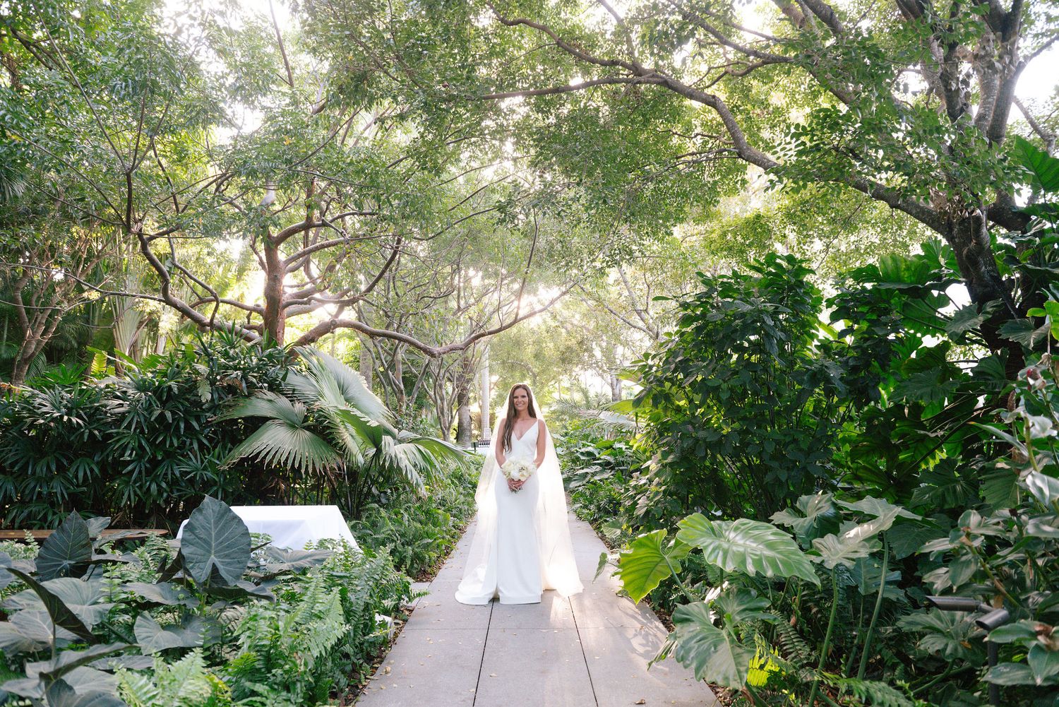 Garden pathway lined with tropical plants and trees creates a natural wedding ceremony backdrop.