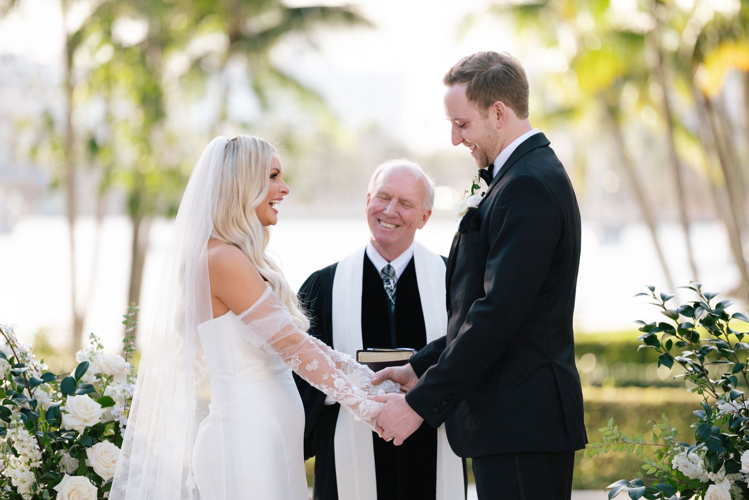 Outdoor wedding ceremony with couple exchanging vows under palm trees by the ocean.
