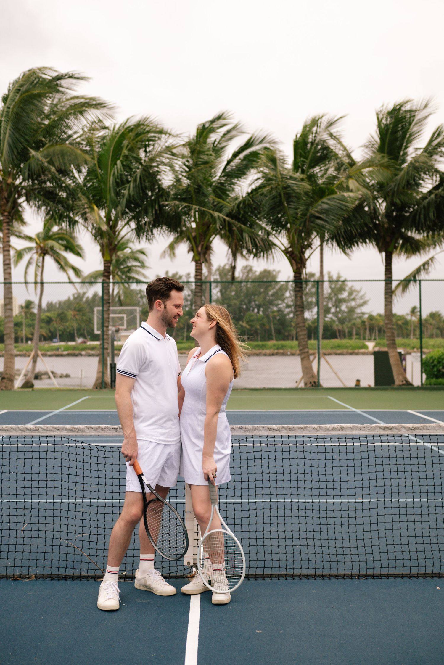 Couple playing tennis together on tropical court surrounded by palm trees.