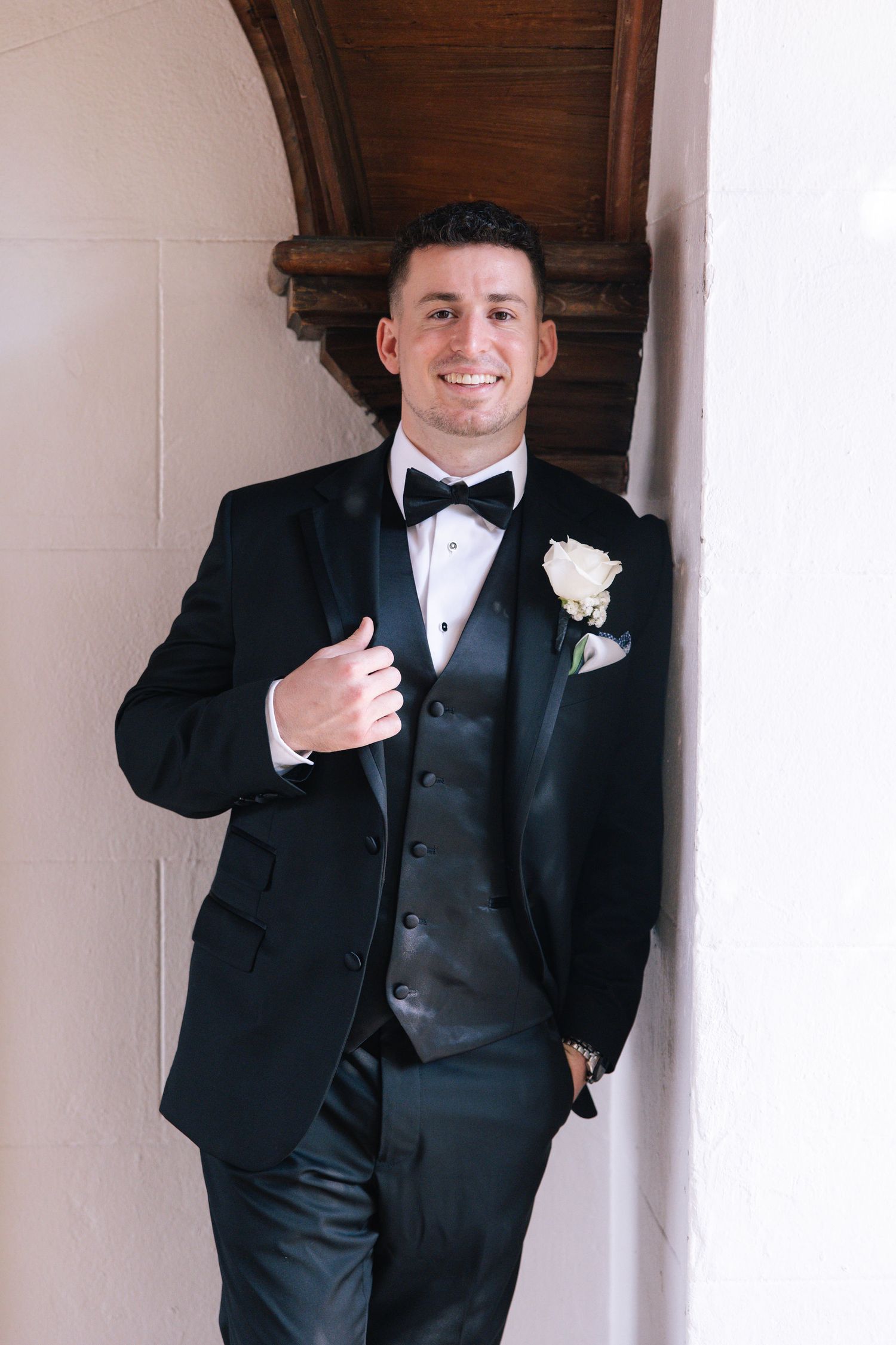 Groomsmen in formal black tuxedos pose in front of white pillars.