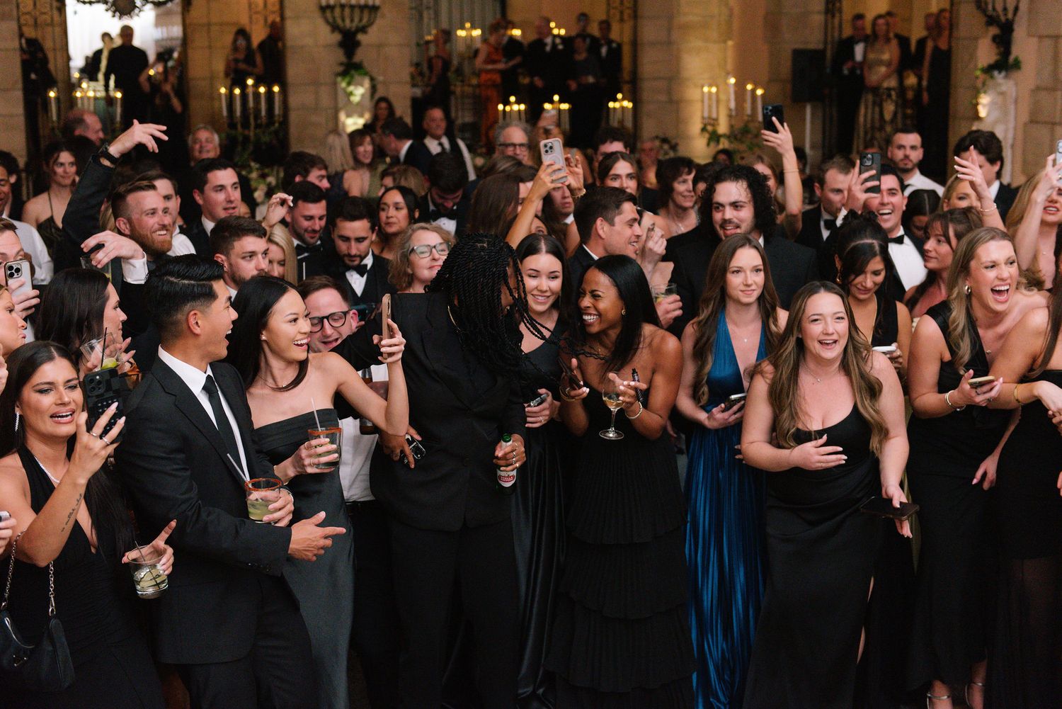 Large crowd of wedding guests in formal attire gathered in an elegant ballroom venue.