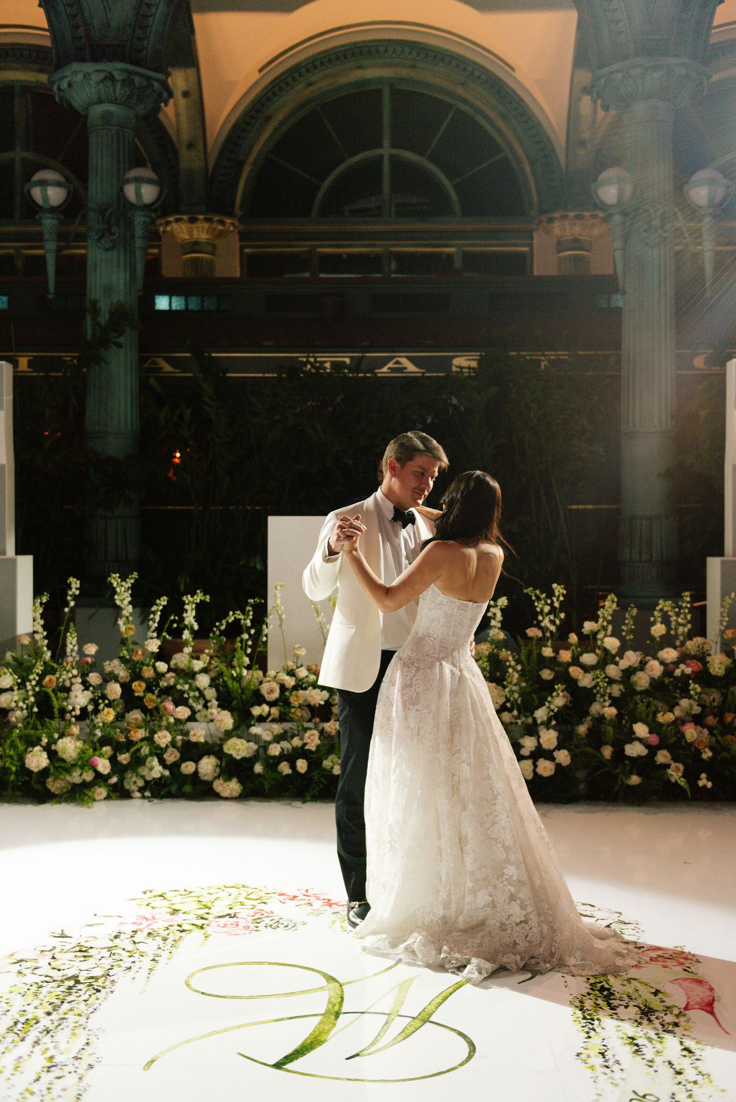 Wedding dance floor decorated with floral arrangements and monogram lighting.