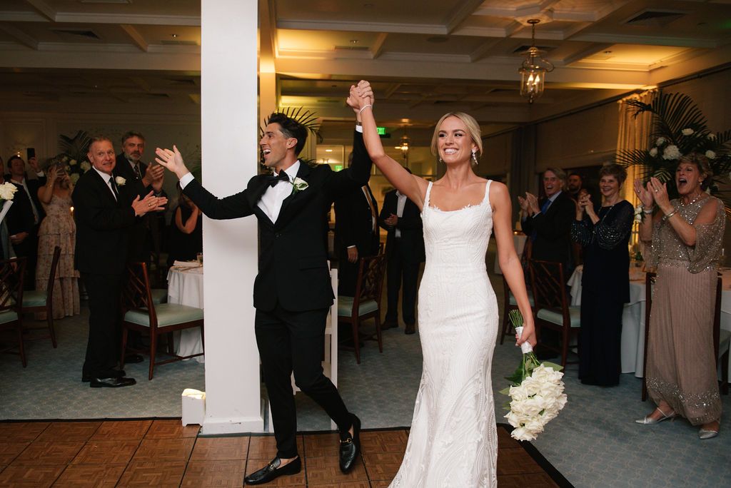 Newlyweds make their grand entrance into a reception hall filled with guests.