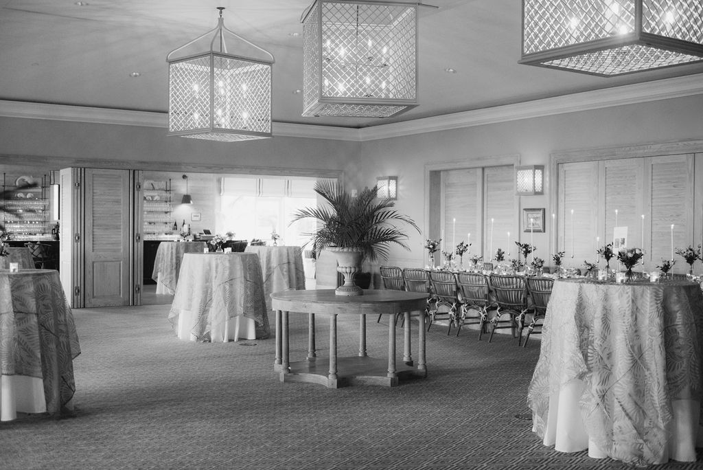 Panoramic view of an empty banquet room with geometric ceiling lights and round tables.